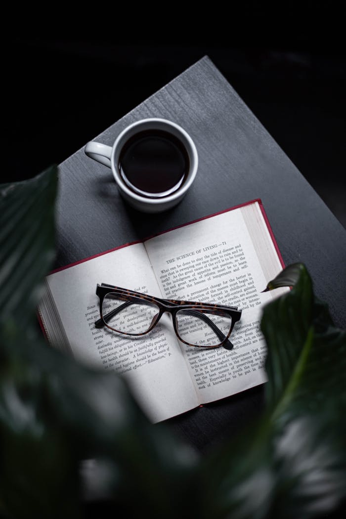 A serene setting with an open book, eyeglasses, and a steaming cup of coffee on a dark table.